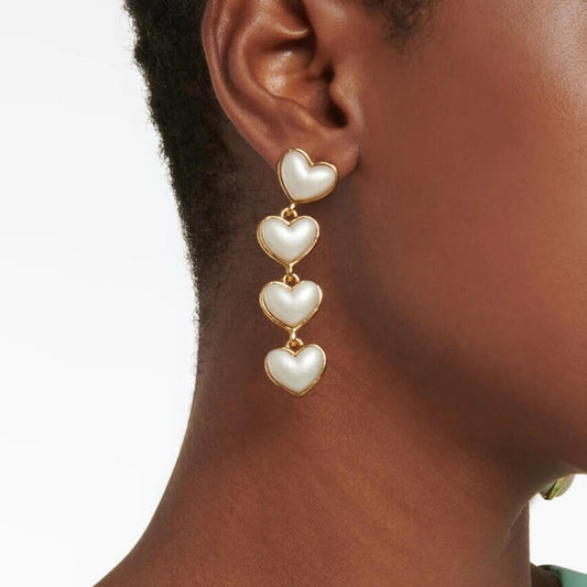 Heart-shaped earrings being worn on an ear with a neutral background