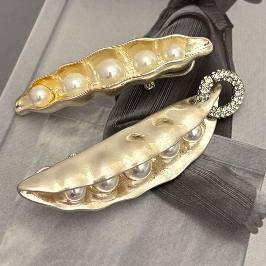 Gold earrings shaped like pea pods with pearls on a gray background