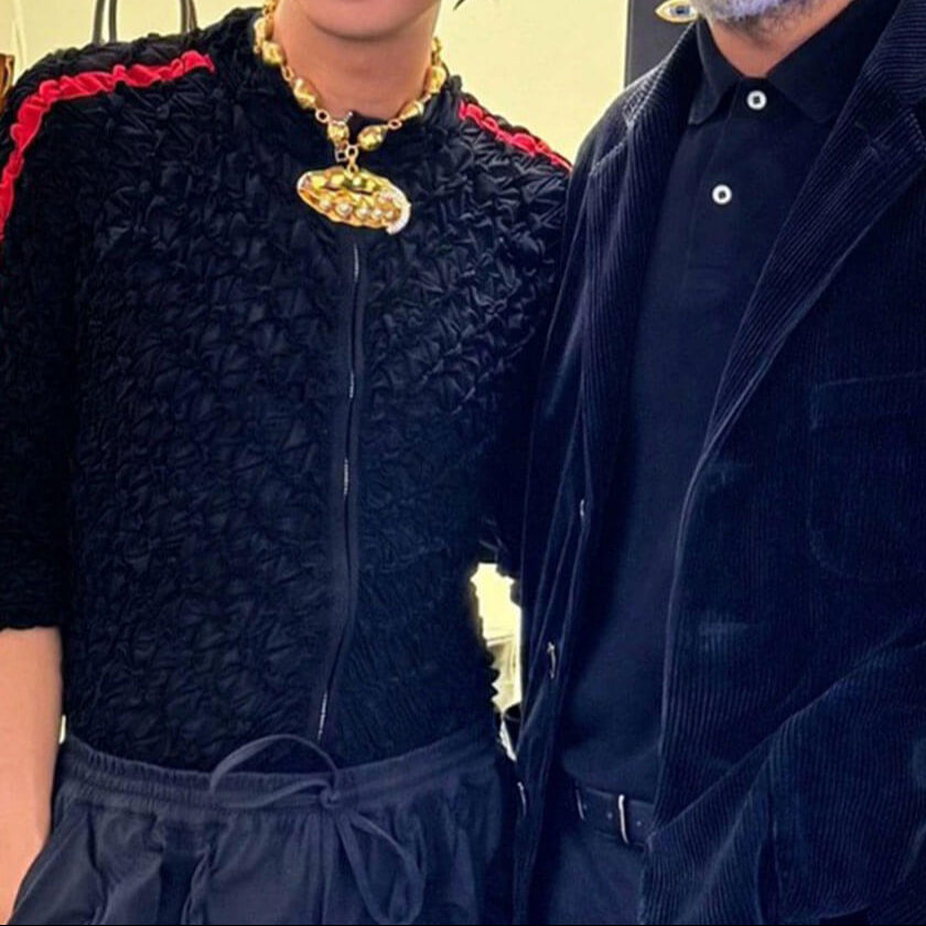 Two people wearing dark clothing with a gold necklace.