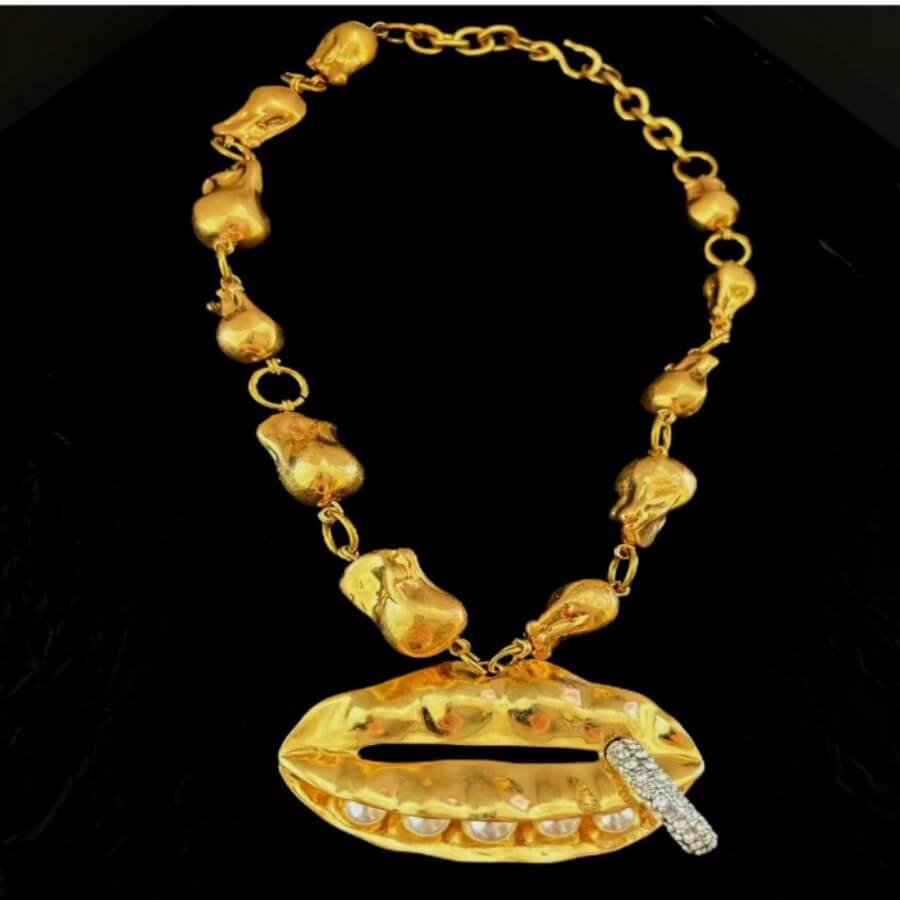 Gold necklace with lip-shaped pendant and chain on a black background