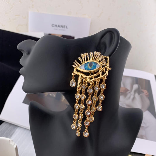 Gold and blue eye-shaped earring on a black mannequin ear with Chanel books in the background