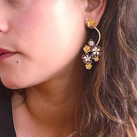 Close-up of a person wearing a floral earring with gold and pink flowers.