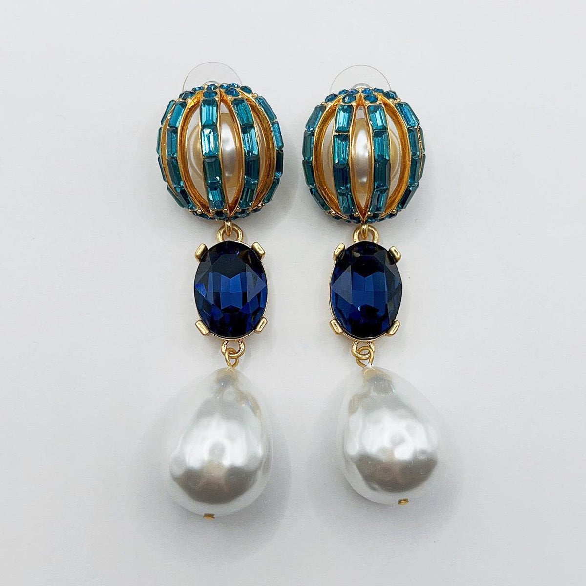 Pair of earrings with blue gemstones and pearl drops on a white background
