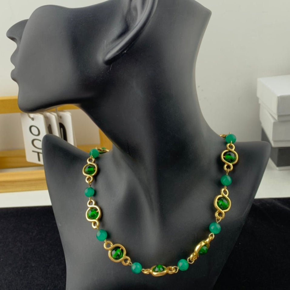 Green and gold necklace on a black mannequin bust with a neutral background