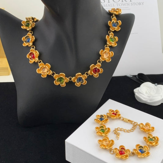Gold necklace with floral design and colored stones on a black stand and white box.